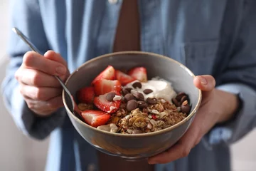 Outdoor kussens Woman eating tasty granola with chocolate chips, strawberries and yogurt, closeup © New Africa
