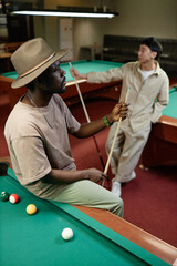Vertical portrait of Black adult man wearing hat posing on pool table in bar