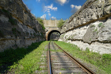 View of the rails going into the distance through an old railway tunnel made of stone between the...