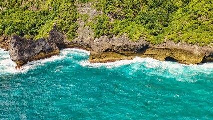 The rocks are washed by white foamy waves. Amazing turquoise seascape. Nusa Penida, Indonesia