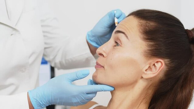 The cosmetologist makes markings on the patient's face. Close-up. Before the procedure of facial contouring or plastic surgery, a mature woman prepares for a cosmetic procedure.