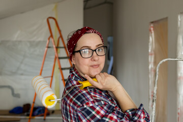 Smiling woman in glasses with a roller in her hands is preparing for painting work. High quality photo