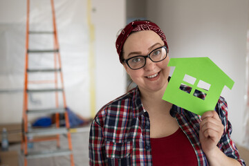 A smiling woman in glasses holds a model of an eco-friendly green house in her hands. High quality photo