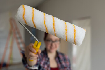A woman points a paint roller towards the camera, the background is out of focus. High quality photo