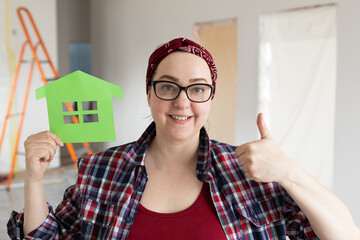 A friendly woman with headbands in her hair and glasses holds in her hands paper seven of a new eco-friendly home. High quality photo