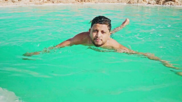 young man floating in bright blue salt pool wearing bathing suit in Siwa Oasis, Egypt