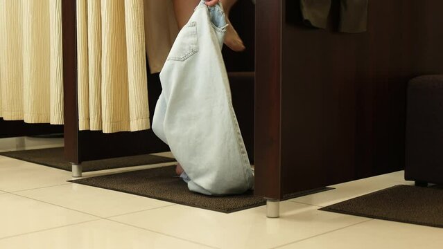 Close-up of woman's legs taking off jeans in store changing room. Shopping for casual clothes in boutique.