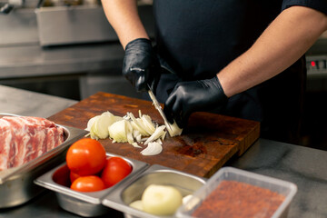 close up in a professional kitchen a chef in a black uniform chops onions on a board