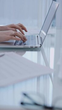 Business woman is working with laptop computer while sitting at the glass table in home office. Female entrepreneur typing information, hands closeup