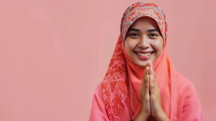 Asian Muslim woman celebrates Eid Mubarak, smiling joyfully in a pink hijab against a pastel background with text space