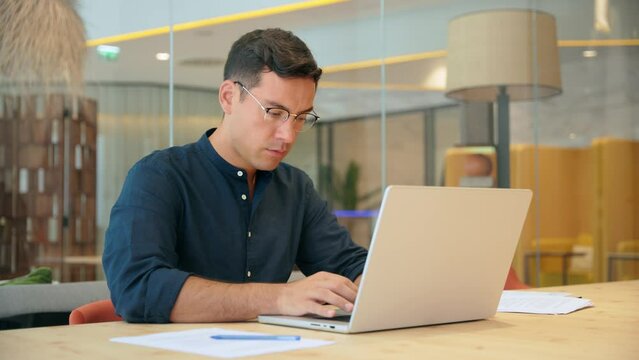 Busy professional business man executive, young male corporate employee, latin businessman wearing glasses typing on computer technology using laptop searching on web working at office workplace desk.