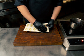 in a professional kitchen hands in black gloves take a delicacy out of a silicone mold