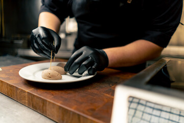 close-up in a professional kitchen chef in black gloves inserts toothpicks into a delicacy - obrazy, fototapety, plakaty