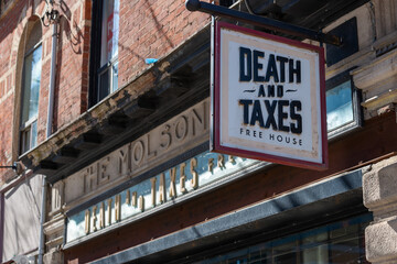Fototapeta premium exterior building and sign of Death & Taxes Free House, a pub, located at 1154 Queen Street West in Toronto, Canada