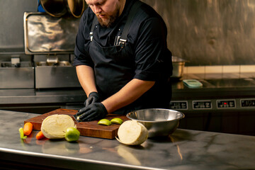 in a professional kitchen wearing black gloves cuts a green apple on wooden board