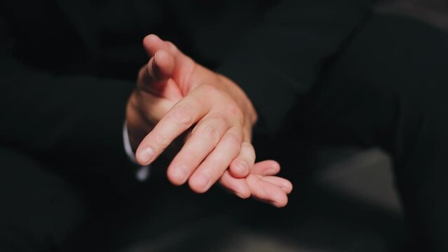 A man is sitting indoors rubbing his hands. He's cupped his hands and he's obviously nervous. Close-up hand shots