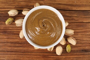 Delicious nut butter in bowl and pistachios on wooden table, top view