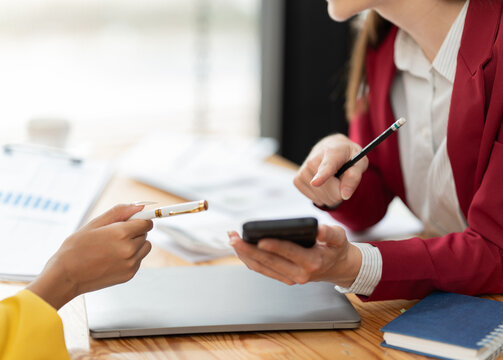 Two businesswomen are actively collaborating in an office setting, engaging in a focused discussion and exchanging ideas while pointing with a pen and holding a mobile phone