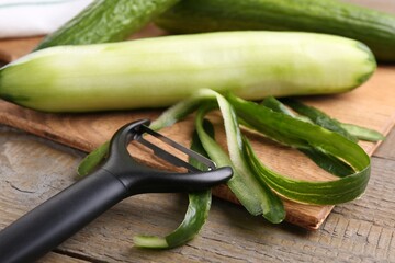 Fresh cucumbers, peels and peeler on wooden table, closeup