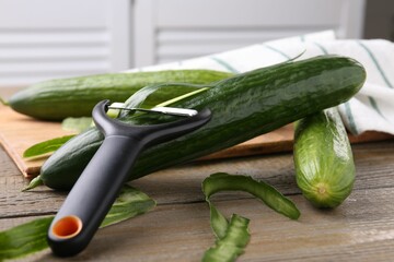 Fresh cucumbers, peels and peeler on wooden table, closeup