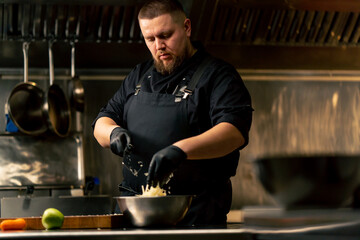 in professional kitchen wearing black gloves pours cabbage into an iron bowl