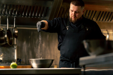 in professional kitchen wearing black gloves salting cabbage in an iron bowl
