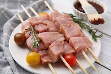 Skewers with pieces of raw meat, rosemary, tomatoes and marinade on rustic wooden table, closeup