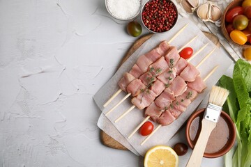 Flat lay composition of skewers with cut raw meat, thyme, tomatoes and marinade on light textured...