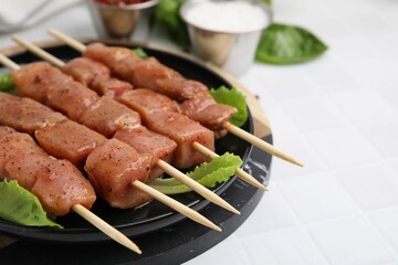 Wooden skewers with cut raw marinated meat on white tiled table, closeup