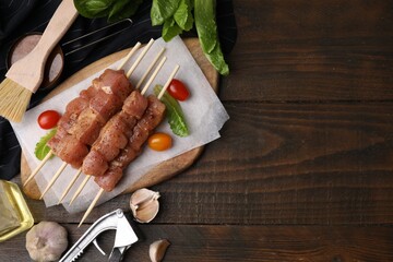 Skewers with cut raw marinated meat on wooden table, flat lay. Space for text