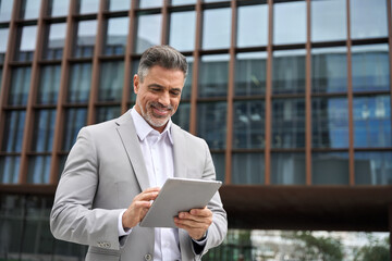 Happy busy middle aged male entrepreneur, rich older investor, confident business man ceo executive leader, mature businessman manager in suit using digital tablet standing outdoors, candid shot. - 783156740