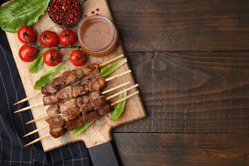 Tasty cooked marinated meat served with sauce and tomatoes on wooden table, flat lay. Space for text