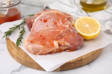 Board with raw marinated meat, lemon and rosemary on white marble table, closeup