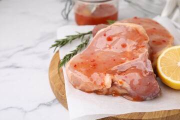 Board with raw marinated meat, lemon and rosemary on white marble table, closeup. Space for text