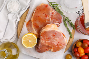 Flat lay composition with raw marinated meat, lemon and rosemary on white table