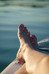 Close-up of a woman's well-groomed, polished foot on a paddleboard in the sunlight on the water in summer. Relaxing.