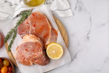 Flat lay composition with raw marinated meat, lemon and rosemary on white marble table. Space for...