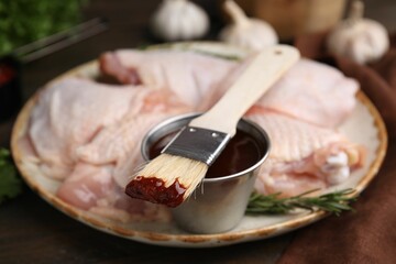 Plate with marinade, raw chicken and basting brush on table, closeup