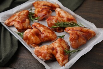Raw marinated chicken wings and rosemary on wooden table, closeup