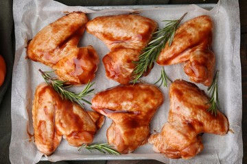 Raw marinated chicken wings and rosemary on table, top view