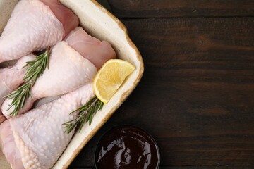 Fototapeta na wymiar Marinade, raw chicken drumsticks, rosemary and lemon on wooden table, flat lay. Space for text