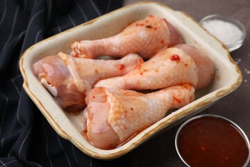 Fresh marinade and raw chicken drumsticks on brown table, closeup