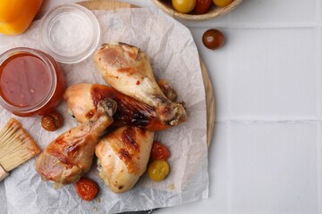 Marinade, basting brush, roasted chicken drumsticks and tomatoes on white tiled table, flat lay....
