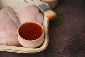Marinade, basting brush and raw chicken fillets on brown table, closeup. Space for text