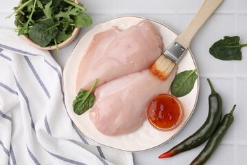 Marinade, basting brush and raw chicken fillets on white table, flat lay