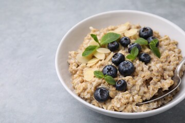 Tasty oatmeal with blueberries, mint and almond petals in bowl on grey table, closeup. Space for text