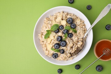 Tasty oatmeal with blueberries, mint and almond petals in bowl on light green background, flat lay. Space for text