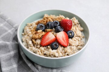 Tasty oatmeal with strawberries, blueberries and walnuts in bowl on grey table