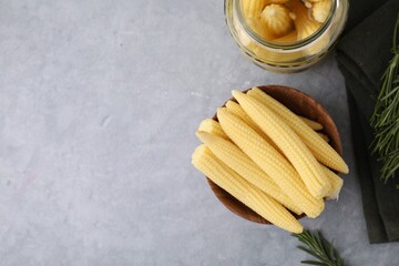 Tasty fresh yellow baby corns in bowl on grey table, top view. Space for text
