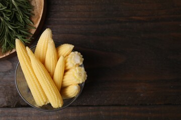 Tasty fresh yellow baby corns in glass on wooden table, top view. Space for text
